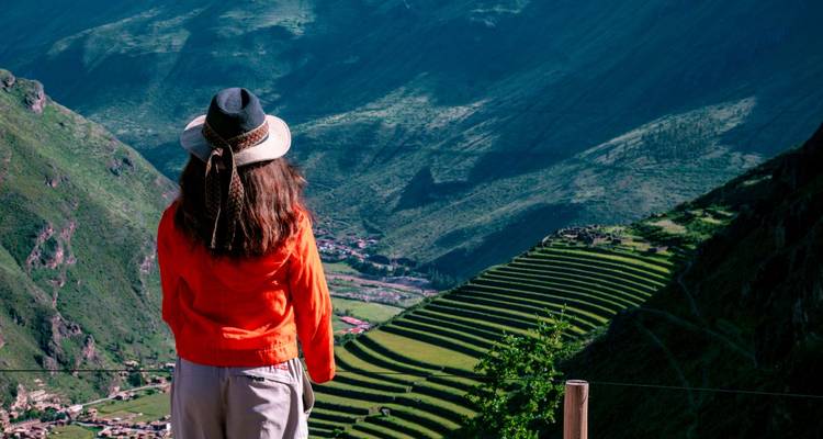 Voyageur en veste et chapeau orange admire la mosaïque de terrasses agricoles vertes qui s'étendent le long d'une haute vallée andine.