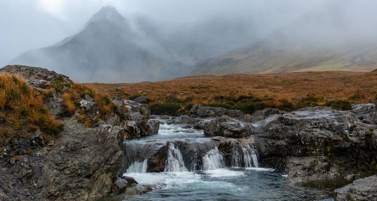 Pic de montagne brumeux et bassins en cascade cristallins des Fairy Pools sur l'île de Skye.