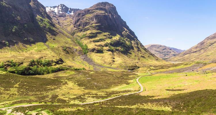Vallée verdoyante balayée par le vent, entourée de pics escarpés et rocheux à Glencoe par une journée lumineuse.