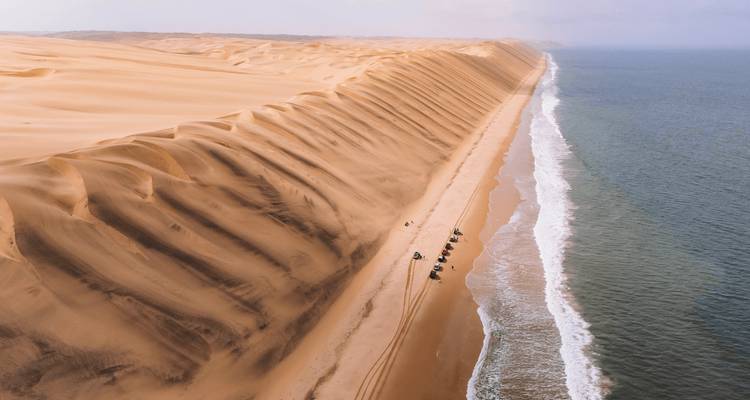 Vue de drone de dunes de sable infinies rencontrant l'Atlantique avec des pistes tout-terrain serpentant le long du rivage.