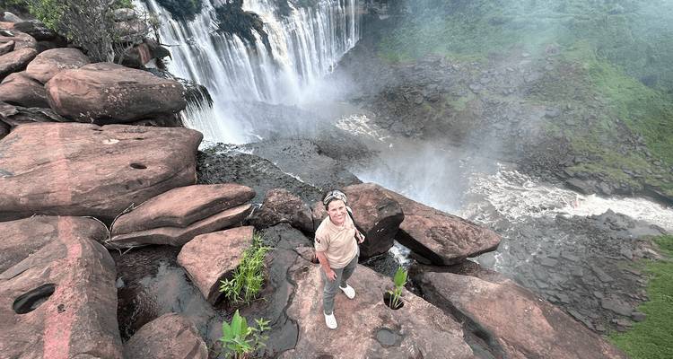 Un voyageur sourit au sommet d'un rebord rocheux à côté d'une cascade rugissante enveloppée de brume.