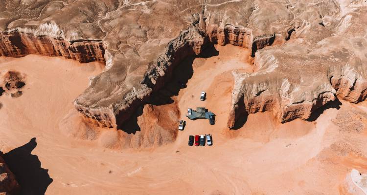 Vue aérienne d'un canyon désertique accidenté où plusieurs véhicules 4x4 sont garés dans un campement isolé.