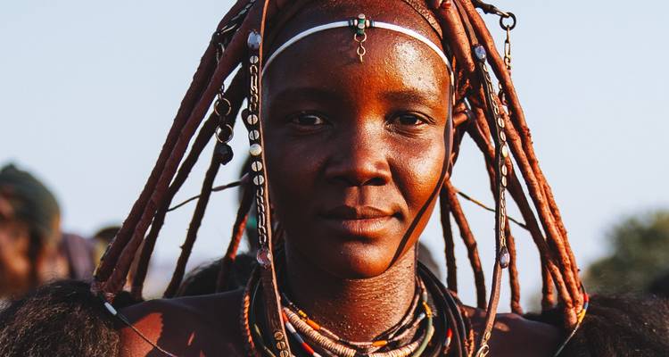 Portrait en gros plan d'une jeune femme himba parée de tresses traditionnelles et de bijoux dans une lumière chaude du soir