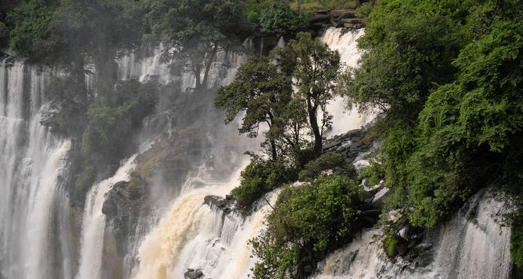 Puissante cascade à plusieurs niveaux dégringolant à travers des falaises boisées d'un vert luxuriant avec de la brume qui s'élève