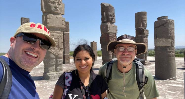 Drei lächelnde Reisende machen ein Selfie mit den steinernen Kriegerstatuen von Tula im Hintergrund an einem hellen Tag
