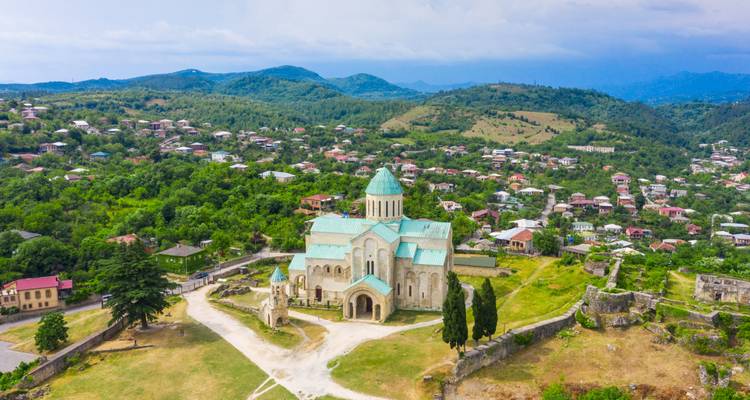 Vista aérea de la Catedral de Bagrati con techo turquesa situada en una colina verde rodeada de exuberante campiña y montañas ondulantes.