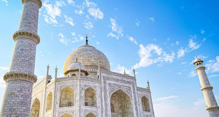 Glorieux mausolée du Taj Mahal en marbre blanc avec des minarets se détachant sur un ciel bleu vif parsemé de nuages.