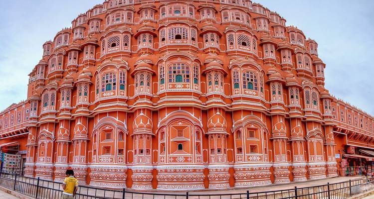 Vue grand angle de la façade ornementée rouge-rose du Hawa Mahal avec un seul visiteur debout en dessous.