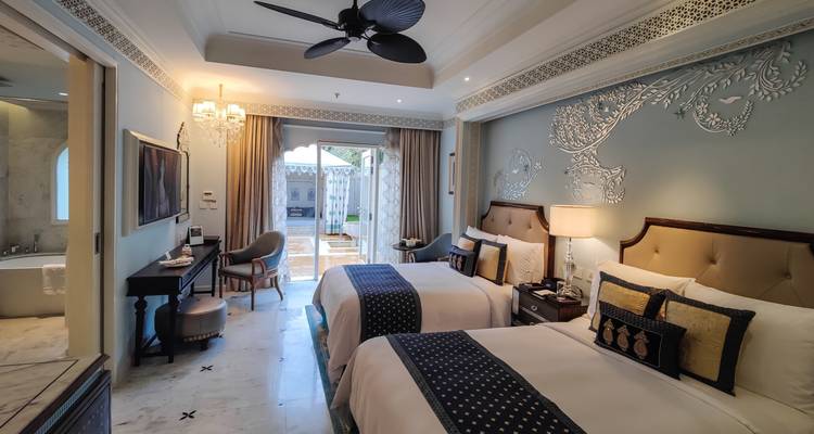 Élégante chambre d'hôtel à lits jumeaux avec décoration ornée, accès au balcon et sol en marbre.