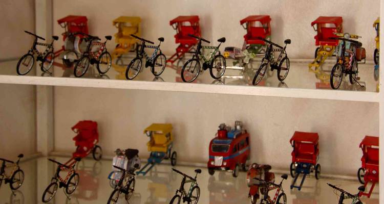 Des étagères exposent des rangées de vélos miniatures, de pousse-pousse et d'autobus jouets dans un atelier local.