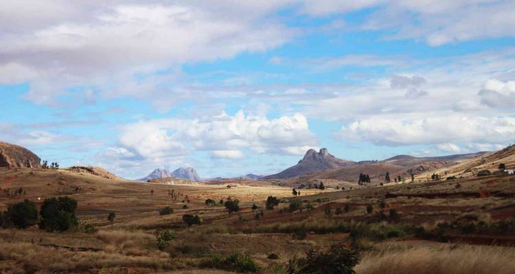 Une vue panoramique des hauts plateaux herbeux de Madagascar avec des affleurements rocheux spectaculaires sous un ciel partiellement nuageux.