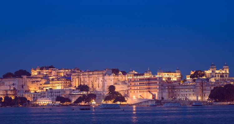 Vue nocturne du complexe du Palais de la Ville d'Udaipur illuminé au bord des eaux calmes du lac Pichola.