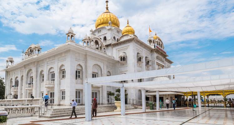 Temple sikh en marbre blanc avec des dômes dorés et des visiteurs marchant à travers une cour carrelée spacieuse à Delhi.
