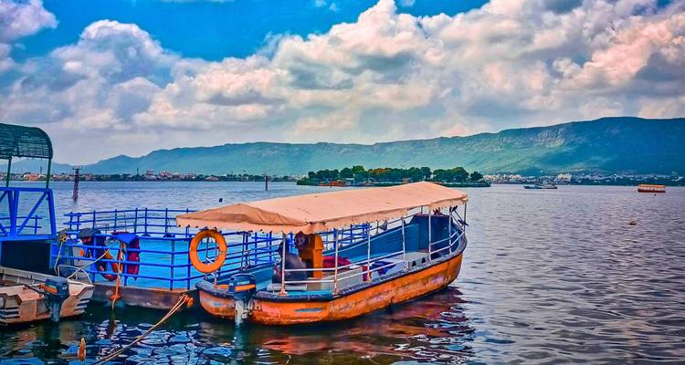 Bateau de passagers coloré amarré sur un lac scintillant avec les collines d'Aravalli et l'horizon d'Udaipur au-delà.