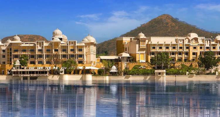 Complexe hôtelier haut de gamme au bord du lac se reflétant dans l'eau calme sur fond de collines Aravalli à Udaipur.