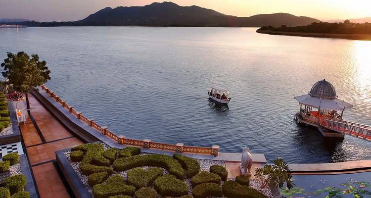 Petit bateau transportant des touristes glisse sur un large lac vers le coucher de soleil près d'une jetée ornée à Udaipur.