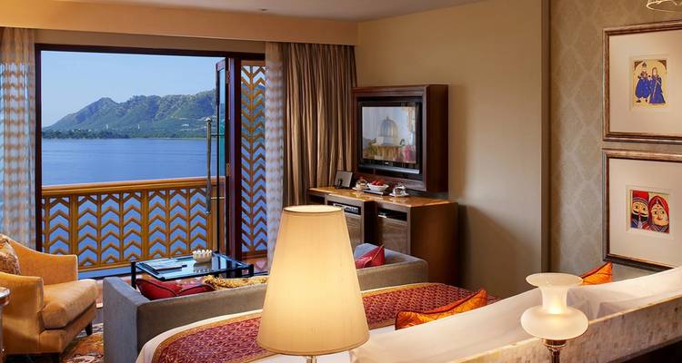 Suite d'hôtel de luxe avec canapé et balcon offrant une vue panoramique sur le lac et les montagnes à Udaipur.