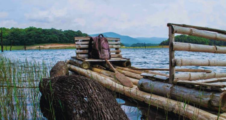 Einfaches Bambusfloss am ruhigen Seeufer festgebunden mit bewaldeten Hügeln dahinter.