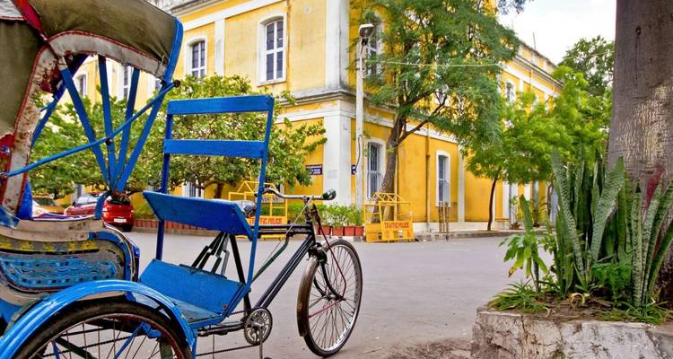Pousse-pousse bleu vif garé à côté d'un bâtiment colonial français jaune au milieu d'arbres verts à Pondichéry.
