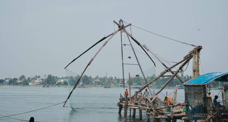 Structure traditionnelle de filet de pêche chinois s'étendant sur les eaux au large de Kochi avec des travailleurs visibles.