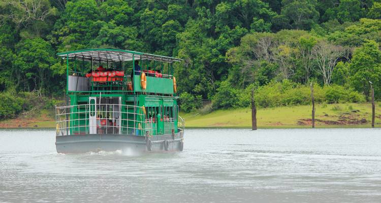 Bateau de safari vert naviguant sur un lac tranquille encadré par des collines densément boisées à Periyār.