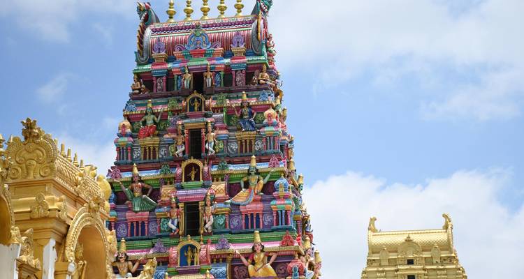 Un gopuram aux couleurs vibrantes, surmonté de kalacha dorées, encadré par le ciel bleu d'un temple du sud de l'Inde.