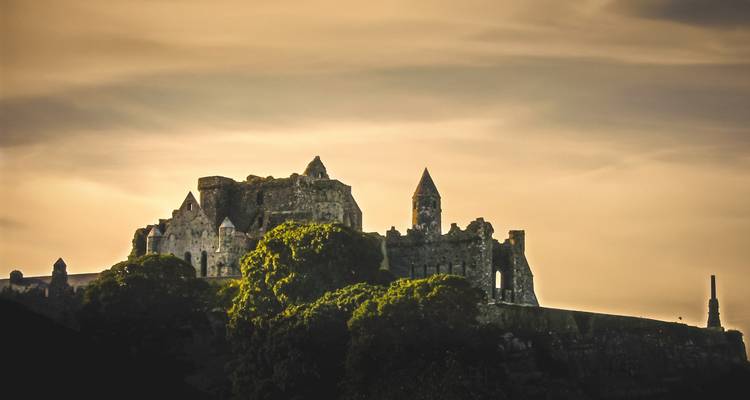 Silhouettierte Ruinen des Rock of Cashel auf einem Hügel vor einem stimmungsvollen goldenen Himmel