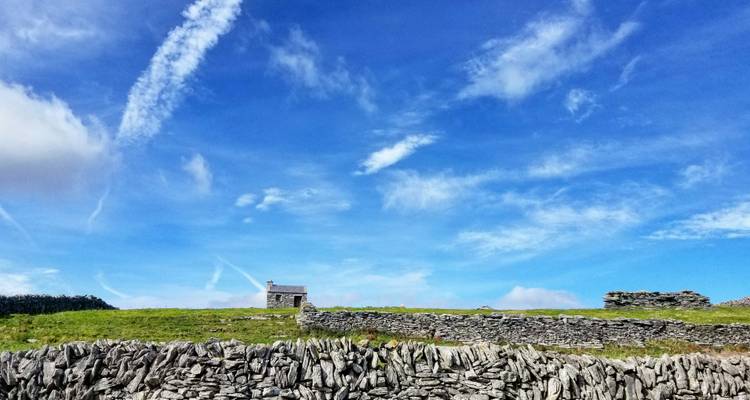 Stone-walled fields and small cottage under expansive blue sky on Inishmore Island