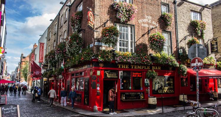 Iconic red Temple Bar pub overflowing with hanging flower baskets on lively cobblestone street