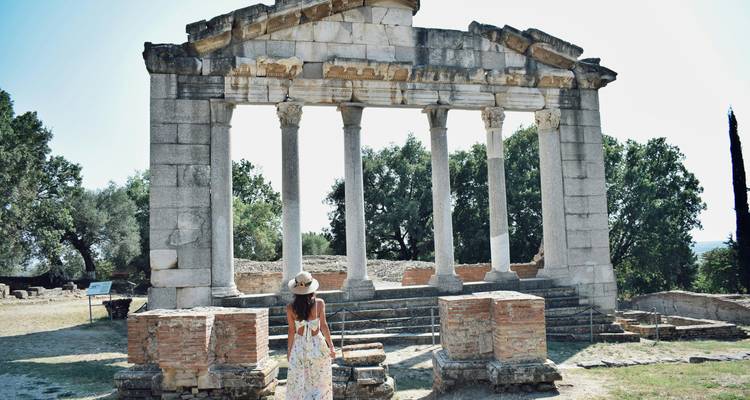 Woman in a floral dress and sun hat gazes at the ancient columned ruins of Apollonia Archaeological Park