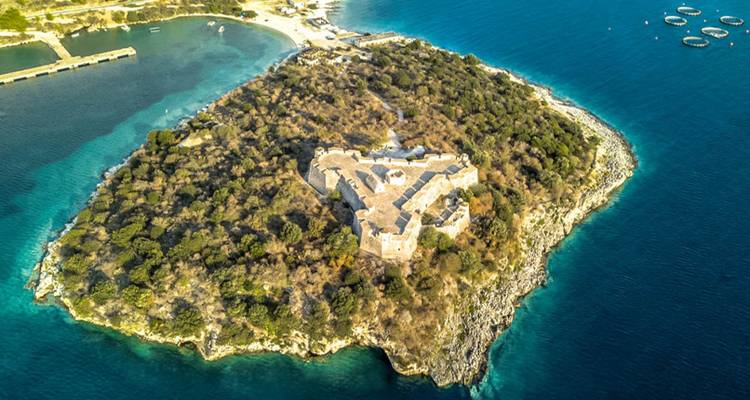 Drone view of a small forested island with a stone fortress surrounded by turquoise sea