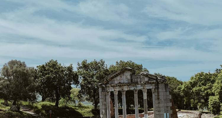 Ancient colonnaded ruins framed by vast sky and surrounding trees