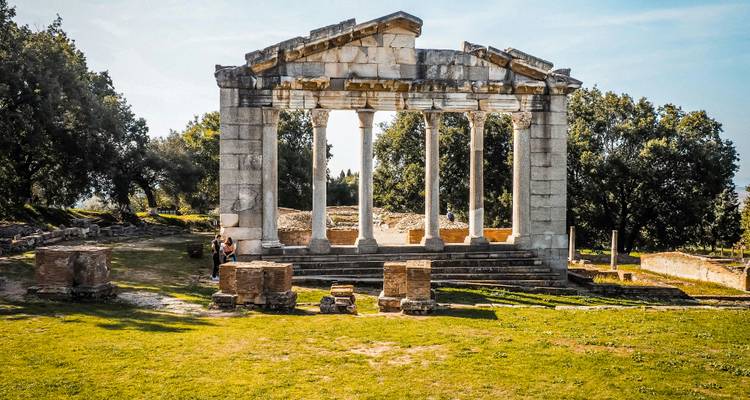 Well-preserved ancient temple remains at Apollonia with visitors exploring the grassy site