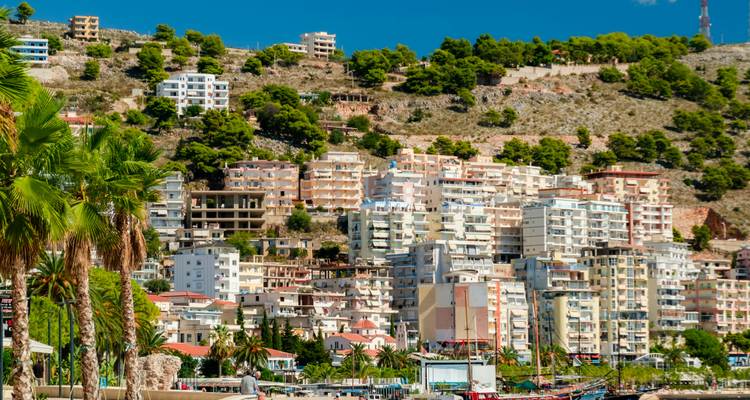 Dense cluster of modern apartments rising up a green hillside under a bright blue sky
