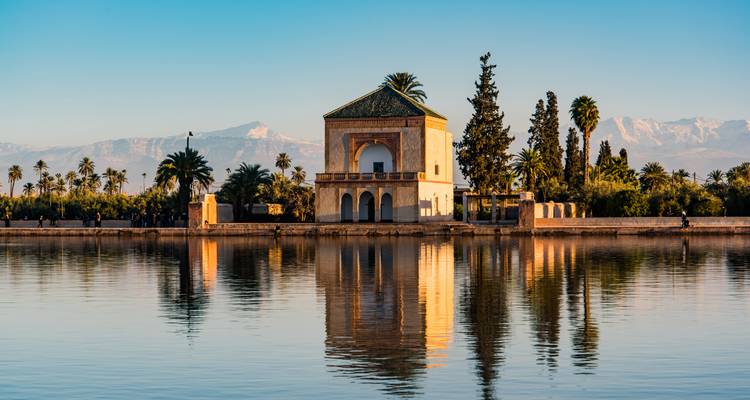 Pavillon élégant aux jardins de Menara reflété dans une eau calme avec les montagnes de l'Atlas en arrière-plan.