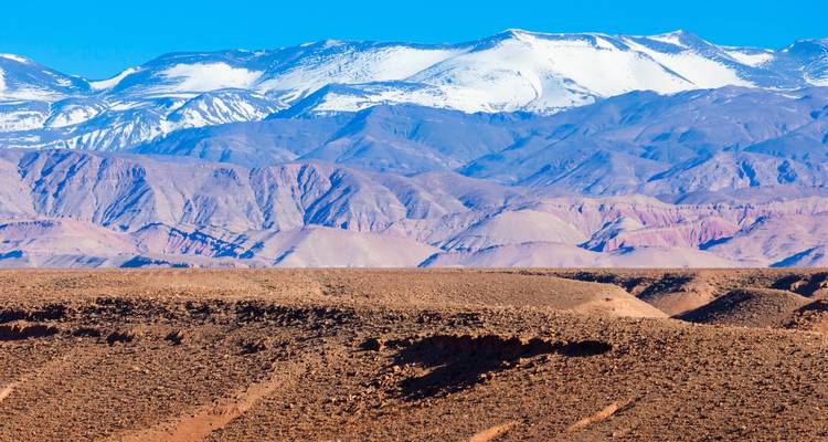 Vue panoramique des montagnes du Haut Atlas enneigées s'élevant au-dessus des contreforts du désert en étages.