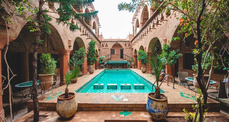 Cour luxuriante d'un riad traditionnel avec un bassin central turquoise et des arcs ornés.