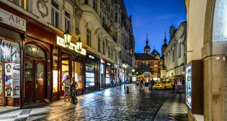 Calle empedrada del casco antiguo en la hora azul con escaparates iluminados y edificios con agujas al fondo