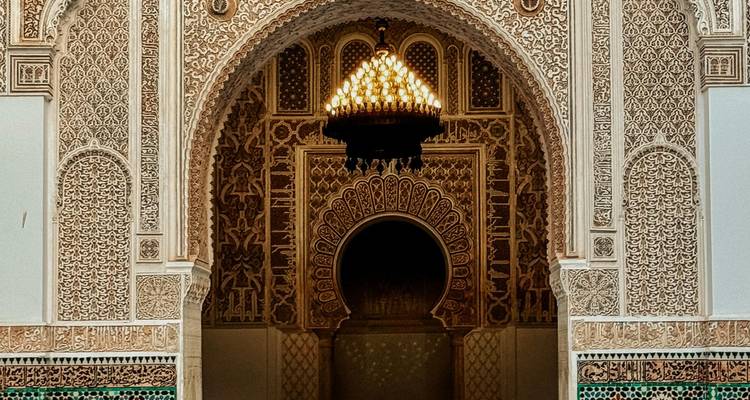 Porche en stuc finement sculpté et lustre à l'intérieur d'une madrasa historique à Fès.