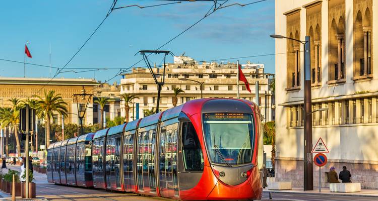 Un tramway rouge moderne glissant dans une rue ensoleillée de Casablanca bordée de palmiers et de bâtiments.