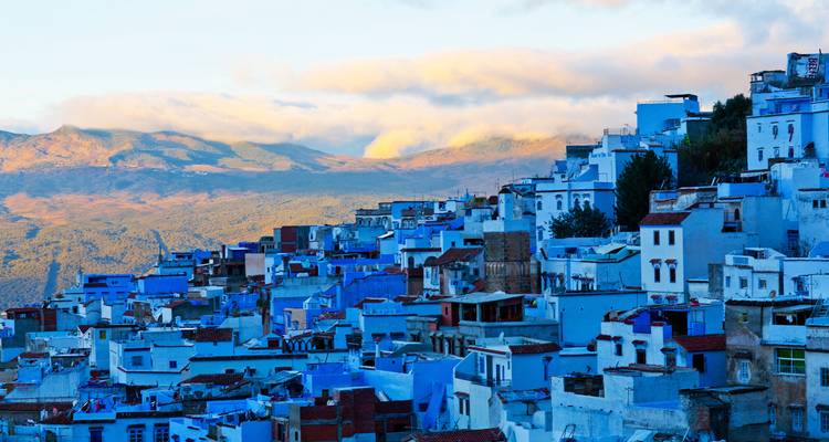 Vue panoramique des maisons peintes en bleu de Chefchaouen sur le flanc de la colline au coucher du soleil avec les montagnes lointaines.