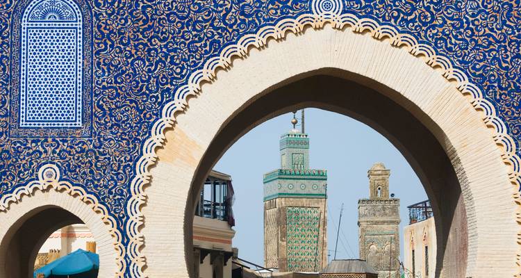 La porte Bab Bou Jeloud aux carreaux bleus encadrant les minarets de la médina de Fès sous un ciel dégagé.