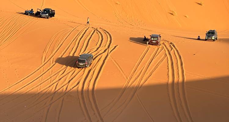 Les véhicules 4x4 et les traces de pneus fraîches traversent les dunes orange imposantes du Sahara près de Merzouga.