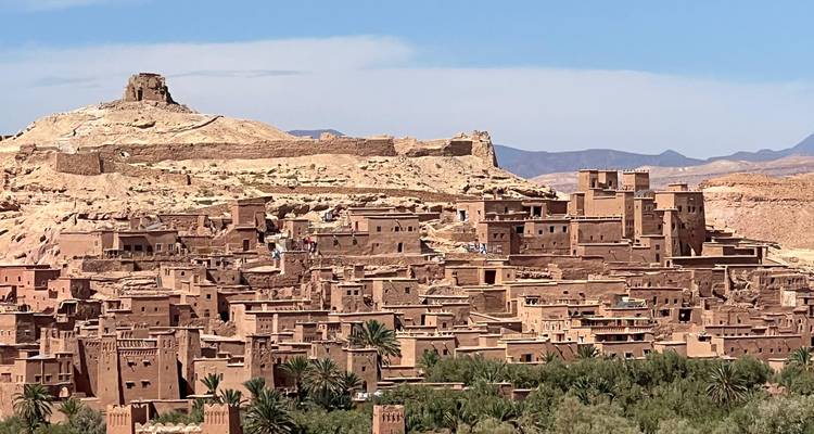 Vue panoramique sur le village de terre fortifiée d'Aït Benhaddou avec des collines arides en arrière-plan.