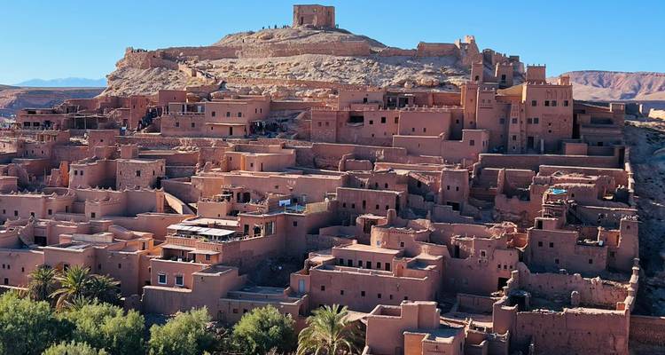 Une citadelle en terre impressionnante et des maisons en adobe regroupées s'élèvent sur une colline rocheuse sous un ciel bleu dégagé