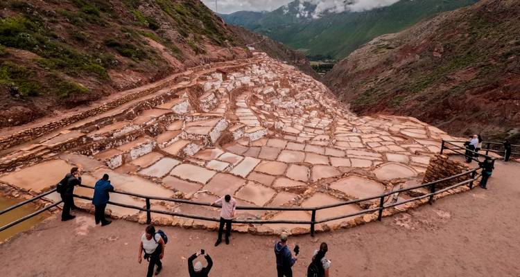 Vue large des bassins de sel en terrasses de Maras avec des visiteurs qui observent et photographient depuis une rambarde en bois