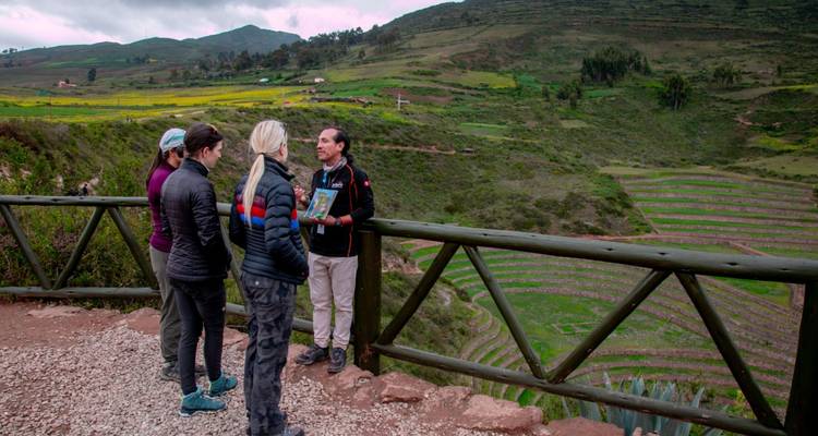 Guide montrant une carte aux voyageurs depuis un belvédère surplombant des terrasses agricoles circulaires vertes dans les hauts plateaux péruviens