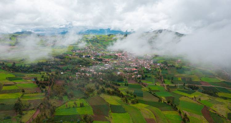 Vue aérienne de terres agricoles verdoyantes en mosaïque et de nuages bas dérivant au-dessus d'un village de vallée des hauts plateaux