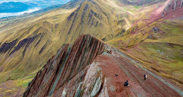 Vista aérea de una cresta montañosa multicolor fina como una navaja con excursionistas empequeñecidos por el vasto paisaje andino.