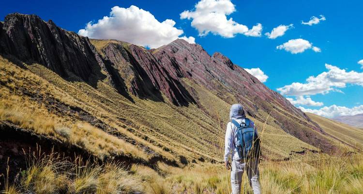 Excursionista solitario con mochila admira la cara estratificada y colorida de una montaña peruana bajo cielos azules.
